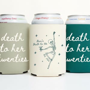 May include: Three beverage can coolers in sage green, cream, and teal. The sage green and teal coolers have the text "death to her twenties" in white script. The cream cooler features a dancing skeleton illustration and the text "Dani's Death to 30s".