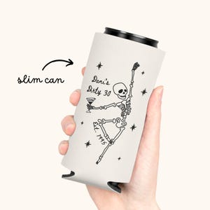 May include: A white slim can cooler featuring a black skeleton design holding a martini glass. The text "Dani's Dirty 30" and "Est. 1995" are also printed on the cooler. The cooler is designed to keep slim cans cold.