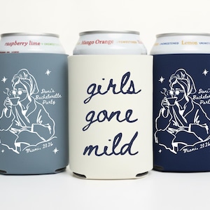 May include: Three beverage can coolers in blue, cream, and navy. The blue and navy coolers feature a white illustration of a woman in a robe, holding a cup. The cream cooler has the words "girls gone mild" in navy script.