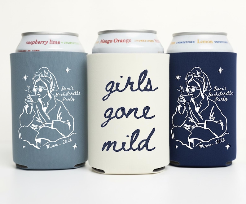 May include: Three beverage can coolers in blue, cream, and navy. The blue and navy coolers feature a white illustration of a woman in a robe, holding a cup. The cream cooler has the words "girls gone mild" in navy script.