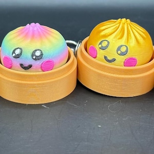 Könnte beinhalten: Sechs farbenfrohe, lächelnde Knödel-förmige Objekte, jeweils in einem kleinen, runden, holzfarbenen Behälter. Die Knödel sind rosa, grün, regenbogenfarben, gelb, lila und blau. Jeder hat ein lächelndes Gesicht mit rosa Wangen und großen Augen.