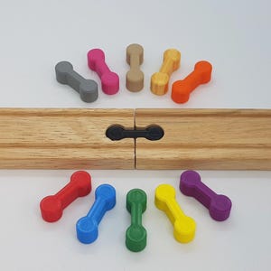May include: A set of ten colorful plastic connectors for wooden train tracks. The connectors are shaped like a dumbbell and come in a variety of colors, including red, blue, green, yellow, purple, orange, pink, gray, and brown.