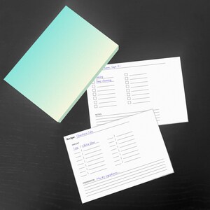 Könnte beinhalten: Ein Stapel rechteckiger Notizkarten mit einem türkis-gelben Farbverlauf sowie zwei bedruckte weiße Karten. Eine Karte zeigt eine Checkliste mit dem Titel "Deep cleaning", die andere ist eine Rezeptkarte mit der Aufschrift "Chocolate Cake".