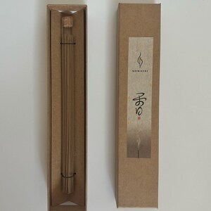 May include: Two rectangular brown cardboard boxes, one open and one closed, on a white surface. The open box contains a glass tube with incense sticks. The closed box has a label with the word "NOWHERE" and Japanese characters.