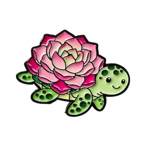 May include: A colourful enamel pin depicting a turtle with a flower shell. The turtle is light green with dark green spots, and the flower is pink and light green. The pin has a black outline.