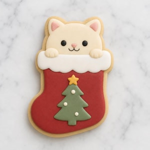 May include: A sugar cookie shaped like a cat peeking out of a red Christmas stocking. The cat is cream-colored with pink inner ears and black eyes. The stocking features a white cuff and a green Christmas tree with a yellow star on top.