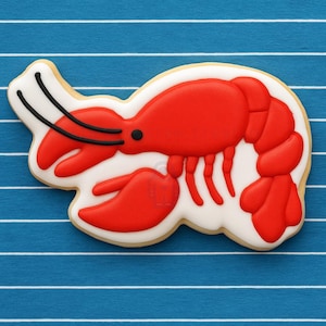 May include: A red and white sugar cookie decorated with icing to look like a lobster. The cookie is on a blue and white striped background.