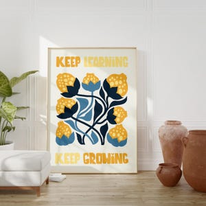 May include: A framed art print featuring a floral design with yellow and blue flowers on a cream background. The words "KEEP LEARNING" and "KEEP GROWING" are printed in yellow. The artwork is displayed in a room with neutral decor.