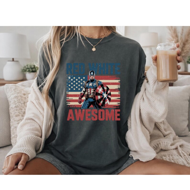 A person wearing a t-shirt with a graphic design featuring a superhero character and the text "RED WHITE AWESOME" printed on it.