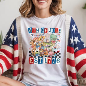 A woman wearing a white t-shirt with a graphic design featuring characters from the Toy Story franchise and the text "4th of July EST 1776".