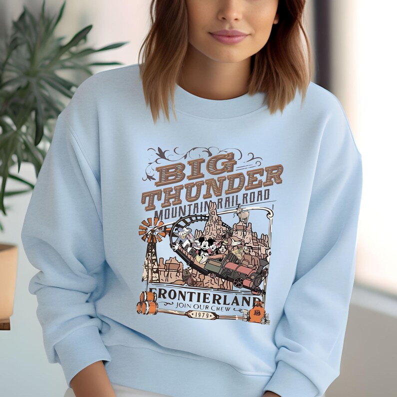 A woman wearing a light blue sweatshirt with a graphic design featuring a train and mountains.