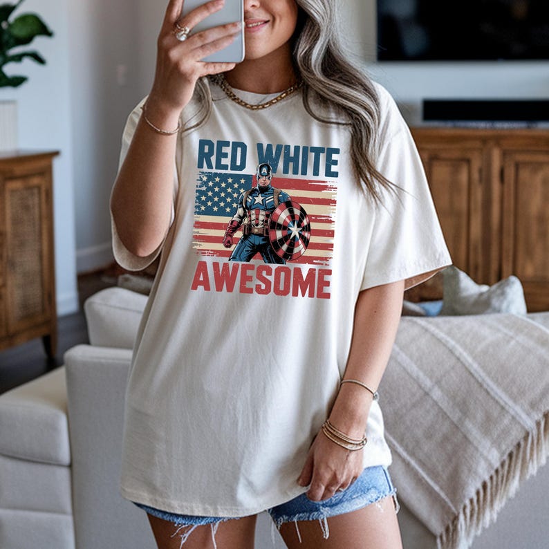 A woman wearing a white t-shirt with a graphic design of a superhero character and the text "RED WHITE AWESOME" printed on it.