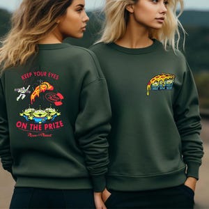 two women wearing green sweatshirts with colorful graphics and text.