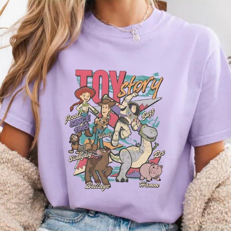 A person wearing a purple t-shirt with a colorful graphic design featuring characters from the Toy Story movie franchise.