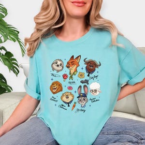 A woman wearing a light blue t-shirt with a graphic design featuring various cartoon animal characters.