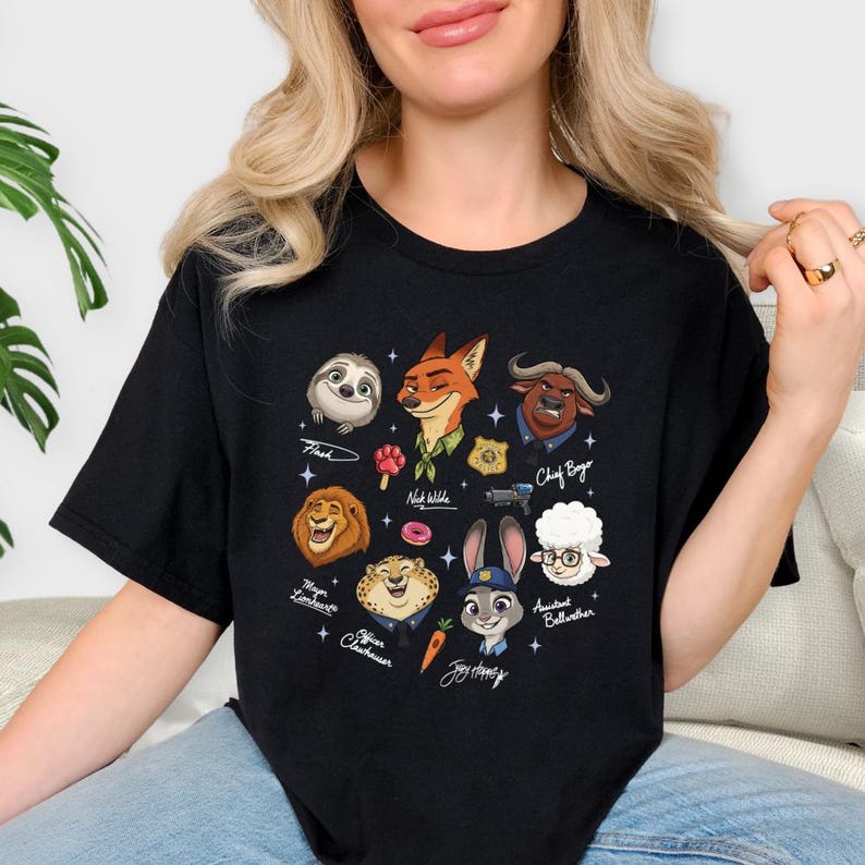 A woman wearing a black t-shirt with a graphic design featuring various cartoon animal characters, including a sloth, fox, lion, unicorn, and other animals.