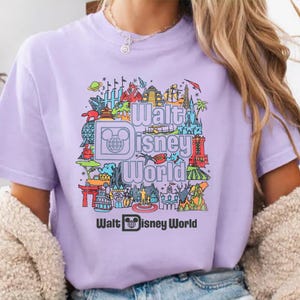 A person wearing a purple t-shirt with a graphic design featuring various Disney landmarks and elements.