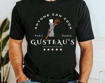 May include: Black t-shirt featuring a cartoon rat chef holding a wooden spoon. The shirt includes the text "Anyone Can Cook" above "GUSTEAU'S" and "Paris France" with five stars below the name.