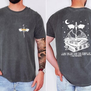 a man wearing a gray t-shirt with a graphic design on the front and back. The design features a dragon and a crescent moon, along with the text "I am the sky and the power of every storm that has ever been, I am infinite".