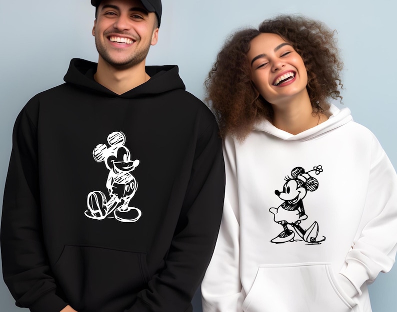 Puede incluir: Sudaderas con capucha en blanco y negro con bocetos de Mickey y Minnie Mouse. La sudadera negra tiene a Mickey Mouse, la blanca a Minnie Mouse. Ambas tienen bolsillo delantero y capucha. Ideales para parejas o fans de Disney.