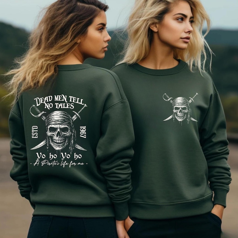 Two women wearing green sweatshirts with pirate-themed designs and text.
