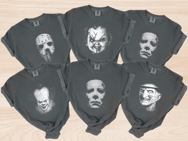 K&ouml;nnte beinhalten: Sechs dunkelgraue T-Shirts mit hochgekrempelten &Auml;rmeln, jeweils mit einem wei&szlig;en Gesicht eines Horrorfilmcharakters. Die Charaktere sind Jason Voorhees, Chucky, Michael Myers, Pennywise und Freddy Krueger.