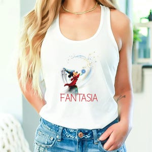 May include: White tank top featuring a graphic of Mickey Mouse as the Sorcerer's Apprentice from Fantasia. The design includes Mickey in a red robe and blue hat, casting a spell with a blue light. The word "FANTASIA" is printed in red.