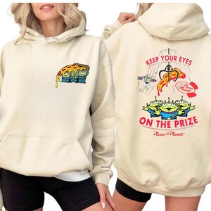 A woman wearing a beige hoodie with a colorful graphic design on the front and back.