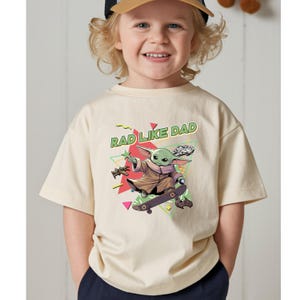 A smiling young child wearing a t-shirt with a graphic of a cartoon character on a skateboard.