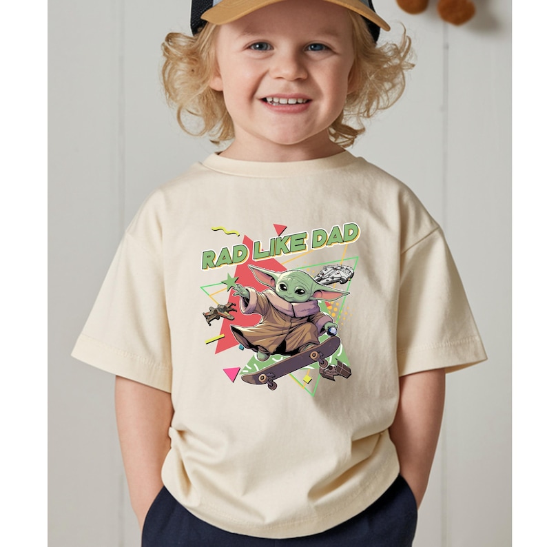 A smiling young child wearing a t-shirt with a graphic of a cartoon character on a skateboard.