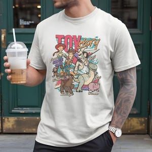 A person wearing a white t-shirt with a colorful graphic design featuring characters from the Toy Story movie franchise.