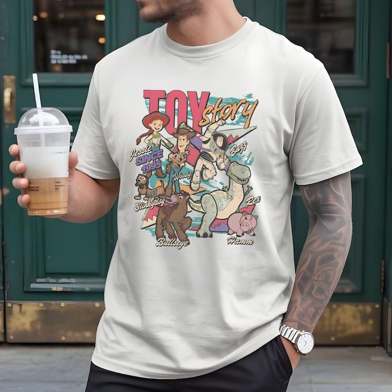 A person wearing a white t-shirt with a colorful graphic design featuring characters from the Toy Story movie franchise.