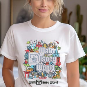 A woman wearing a white t-shirt with a colorful graphic design featuring various Disney-themed illustrations.