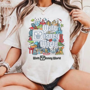 A person wearing a white t-shirt with a colorful graphic design featuring various Disney landmarks and elements.