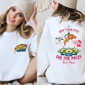A woman wearing a white sweater with a cartoon pizza design and text on the back.