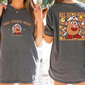 a woman wearing a gray t-shirt with a design of a cartoon character resembling Mrs. Potato Head from the Toy Story franchise.