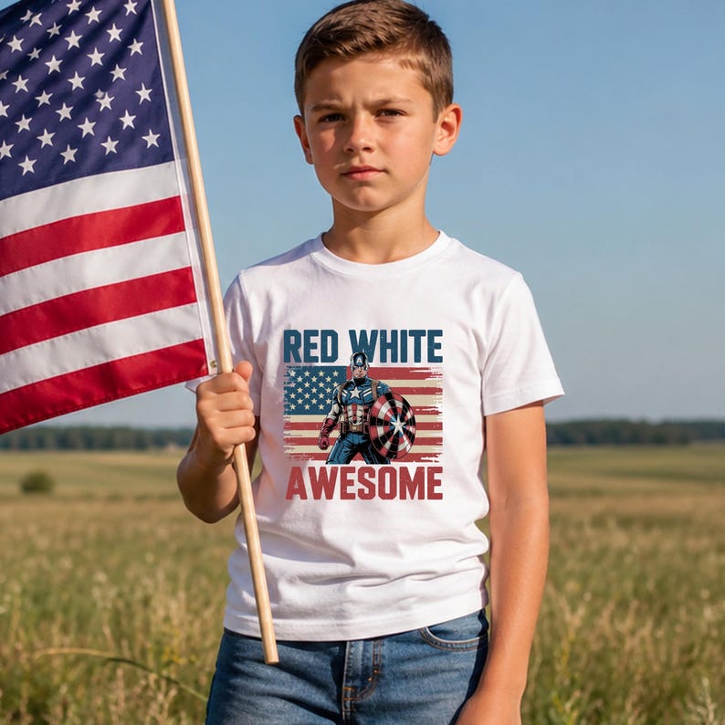 A young boy stands in a field, holding an American flag and wearing a t-shirt with a graphic of Captain America and the text "Red White Awesome".