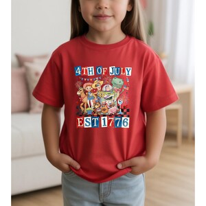 A young girl wearing a red t-shirt with a colorful graphic design celebrating the 4th of July.