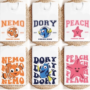 May include: White t-shirts featuring characters from "Finding Nemo." Designs include Nemo, Dory, and Peach, with text like "NEMO," "DORY," and "PEACH." Each design includes the text "EST 2003" and "FINDING NEMO."