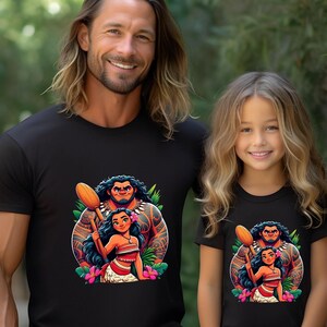 May include: Black t-shirts with a vibrant cartoon illustration of a Polynesian man and woman with a flower and leaf design. A man and a young girl are wearing the shirts, both smiling.