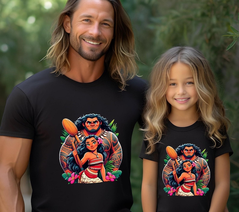 May include: Black t-shirts with a vibrant cartoon illustration of a Polynesian man and woman with a flower and leaf design. A man and a young girl are wearing the shirts, both smiling.