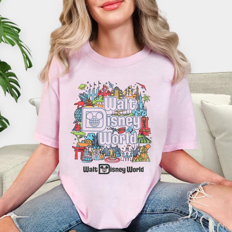 A woman wearing a pink t-shirt with a colorful graphic design featuring various Disney landmarks and characters.