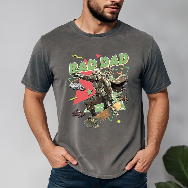A man wearing a gray t-shirt with a graphic design featuring a character riding a skateboard and the text "RADDAD" prominently displayed.