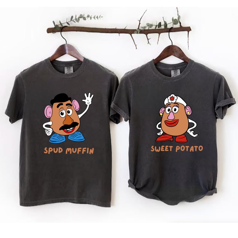 two gray t-shirts with cartoon characters on them, hanging on a wooden hanger.