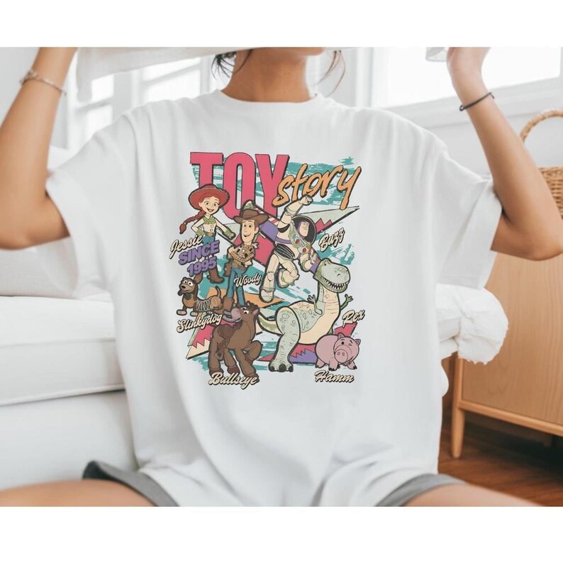 A person wearing a white t-shirt with a colorful graphic design featuring characters from the Toy Story movie.