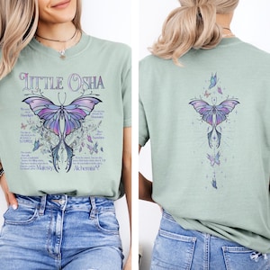 A woman wearing a green t-shirt with a butterfly design and text printed on it.