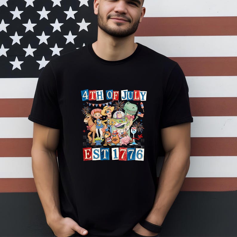 A man wearing a black t-shirt with a graphic design of various cartoon characters and fireworks, standing in front of an American flag.
