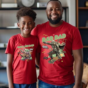 A young boy and an adult man wearing red t-shirts with a graphic of a character from the Star Wars franchise, specifically the character Baby Yoda.