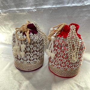 Peut inclure: Deux pochettes à cordon, l'une violet foncé et l'autre rouge vif, ornées de broderies florales argentées, de perles blanches et d'une large bordure tissée en or métallique à la base, avec des poignées en cordon doré assorties.
