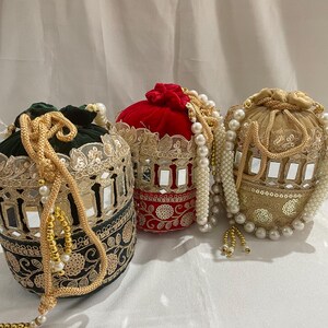 May include: Three decorative drawstring bags in green, red, and gold. Each bag features intricate embroidery, mirror accents, and beaded embellishments. The bags have a round shape and are likely used for carrying small items.